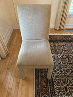 Front view of beige upholstered contemporary dining chair showing entire chair including high back and four fabric-wrapped legs.
