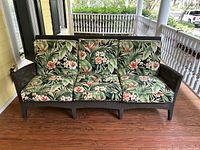 Front view of dark brown wicker sofa with floral cushions showing three seat and back cushions with a tropical floral pattern.