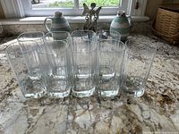 Front view of nine clear glass drinking glasses aligned in a row, showing their square-like shape and clear glass material.