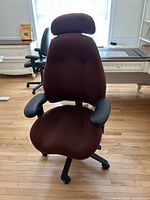 Front view of ergonomic maroon office chair showing padded seat and back, adjustable armrests, and cushioned headrest.