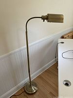 Full view of brass finish floor lamp standing near a white wall with a wooden-panel lower wall and a white desk.