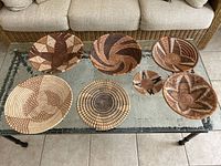 All seven hand woven African decorative bowls arranged on glass table showing variations in size and geometric pattern designs