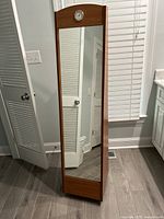 Front view of the light wood floor mirror showing the rectangular reflective surface and built-in analog clock set in the top wooden frame section.