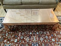 Top-down view of the rectangular glass coffee table showing some scratches and dents on the copper frame and glass surface.
