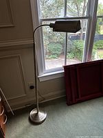 Full view of silver metal floor lamp standing next to window showing height and base detail.