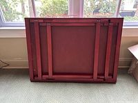Bottom view of the folded red wooden puzzle table showing folding legs and support structures.