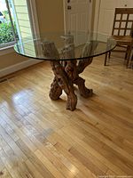 Round glass dining table showing full top and grapevine wood base from an angle