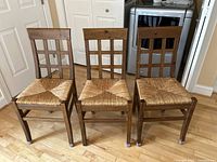 Full set of three farmhouse-style kitchen chairs arranged side by side on hardwood flooring, showing wood frame, woven wicker seats, and grid pattern backrests.