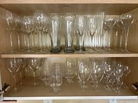 Shelf with multiple rows of clear glassware including wine glasses, water glasses, and champagne flutes
