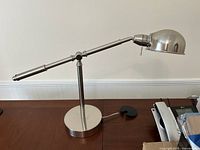 Silver modern adjustable table lamp placed on wooden desk, showing side view with arm extended.