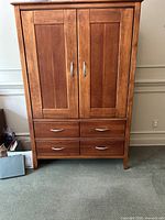Front view of the wooden armoire showing two doors and four drawers with metal handles, medium brown finish.