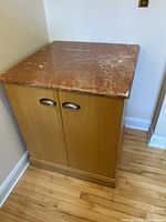 Front view of wood cabinet with marble top and double doors with metal handles.