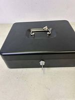 Closed black metal cash box with handle and key lock on front