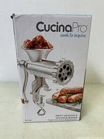 Box front showing CucinaPro Meat Grinder & Sausage Maker, metal grinder image with clamp and food illustrations