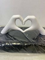 Front angle photo of white ceramic hands sculpture forming a heart shape on a black surface.