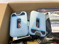 Photo showing two Yeti Thin Ice reusable ice packs and a clear plastic bag with black hose labeled XHose Pro DAC-5 fiber high performance hose