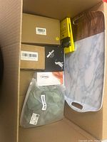 Box with multiple cardboard boxes and a marble-effect serving tray with wooden handle on side