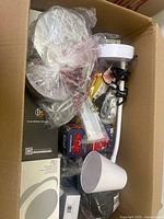 Top view of box showing clear plastic bowls or light covers, white containers, and other assorted hardware and electronic items in packaging.