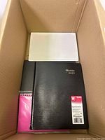 View of Brownline 2025 weekly appointment book with a white item and small pink spiral notebook