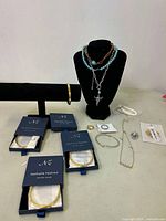 Full shot showing the assortment of new costume jewelry including bracelets in boxes, necklaces on bust, earrings, and loose bracelets and chains on table