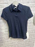 Front view of Lululemon women's navy blue polo top on hanger showing collar, button placket, short sleeves, and Lululemon logo on chest.