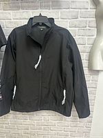 Full front view of the men's black Coal Harbour jacket hanging on a hanger, showing the zipper, collar, and zippered pockets with white zipper pulls.