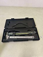 Open carrying case showing digital caliper inside along with metal ruler, caliper turned on displaying measurement on LCD.
