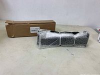 6 black metal shelf brackets wrapped in bubble wrap, placed on a white surface with opened cardboard box behind