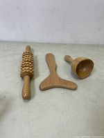 Wooden massage tools set including roller massager, T-shaped gua sha, and dome hand massager shown from above on a neutral surface.