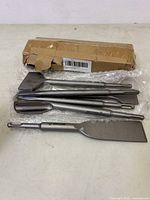 Photo of six different chisels with SDS Plus shanks laid out on a bubble wrap sheet, accompanied by a damaged cardboard box.