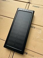 Close-up of a single black solar power bank showing solar panel surface and carbon fiber textured border.