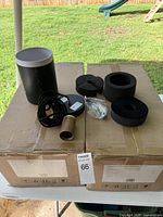 Various components of the pendant light including bulb holder with walnut wood finish, black ceiling rose plate, cable, and mounting accessories on top of the cardboard boxes of the lot.