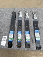 Four 20-inch black metal mower blades, three wrapped partly in plastic with labels visible, one unwrapped.