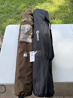 Two camping chairs in their carrying bags on a table outdoors on grass, one brown Realtree Edge camo chair bag and one black Quest branded bag.