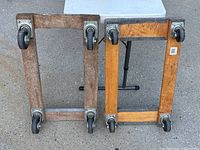 Top view of two rectangular wooden furniture dollies with metal swivel caster wheels on asphalt surface.