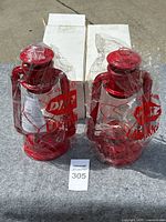 Two red metal lanterns new in original plastic wrap, shown with white retail boxes behind.