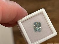 Blue radiant brilliant cut moissanite gemstone shown inside a white display box, clear visible sparkle and color.