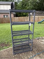 Full view of the 5 tier black plastic shelving unit outdoors showing its structure and condition.