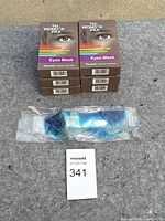 Six unopened boxes of WonderPax reusable eye masks stacked and one blue gel eye mask sealed in plastic in front.