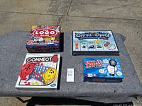 Four board games displayed on a table outdoors: The Logo Game, Detroit-Opoly, Connect 4, Rhyme Antics, showing front box artwork.