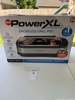 Front of the product box showing PowerXL Smokeless Grill Pro with product features and size details.
