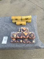 View of 7 small chocolate-themed scented candles in packaging and 3 beige rectangular candles on a gray surface.