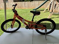 Full profile side view of an orange Cannondale youth bicycle showing frame, tires, seat, and kickstand.