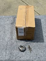 Closed cardboard box containing 50 disc locks, with one disc lock and key displayed in front of the box on a carpeted surface.