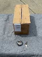 Closed cardboard box containing 50 disc locks, shown with one disc lock and key in front for scale and reference.