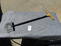 Full view of Fiskars edging tool on grey surface, showing T-shaped yellow handle and metal blade for edging.