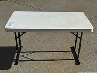 Full view of table showing white plastic top and black metal adjustable height legs with crossbar support.