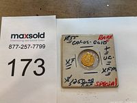 Coin in cardboard holder with handwritten annotations and MaxSold lot card