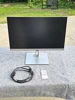Front view of HP 21-inch monitor with power cable placed next to it on a grey surface outdoors.