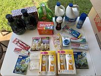 Photo showing entire lot of cleaning and personal care products laid out on a white table outdoors with grass background.